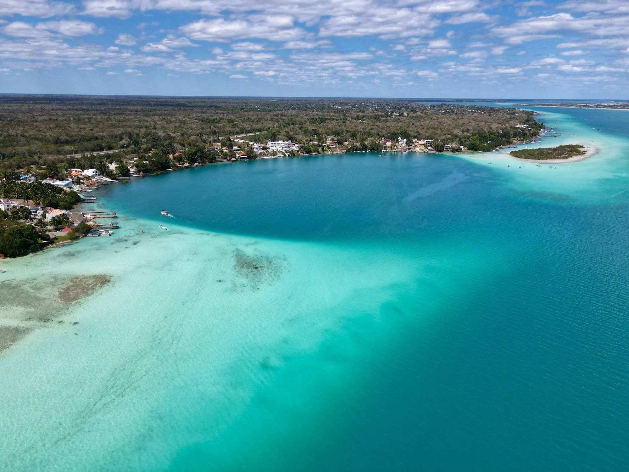Turquoise water and the forested shoreline of Bacalar Lagoon in Mexico.